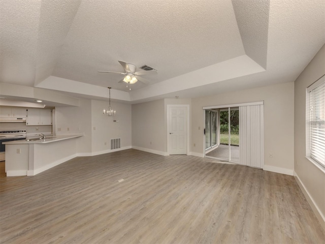 unfurnished living room featuring ceiling fan with notable chandelier, a textured ceiling, and a tray ceiling