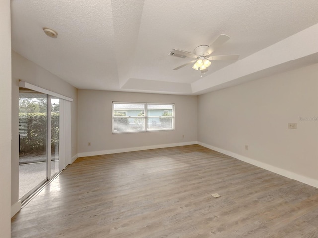 spare room with light hardwood / wood-style floors, a textured ceiling, a raised ceiling, and ceiling fan