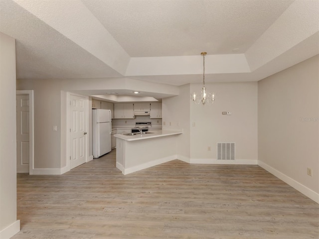 kitchen featuring white refrigerator, hanging light fixtures, kitchen peninsula, a chandelier, and a raised ceiling