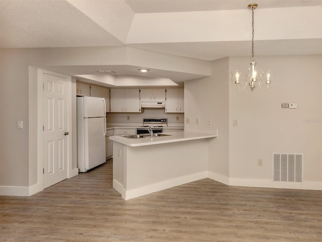 kitchen with decorative light fixtures, wood-type flooring, white fridge, sink, and kitchen peninsula