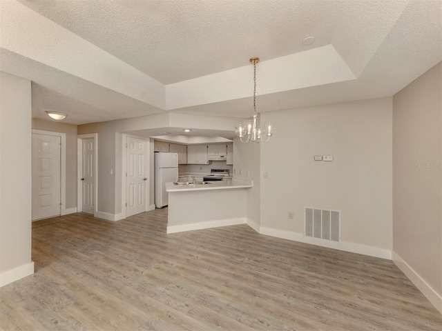 unfurnished living room featuring light hardwood / wood-style floors, a textured ceiling, a raised ceiling, and an inviting chandelier