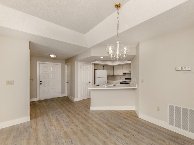 kitchen featuring kitchen peninsula, white appliances, pendant lighting, and a textured ceiling