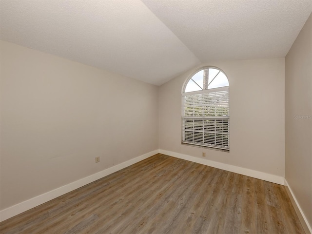 empty room featuring wood-type flooring, a textured ceiling, and lofted ceiling