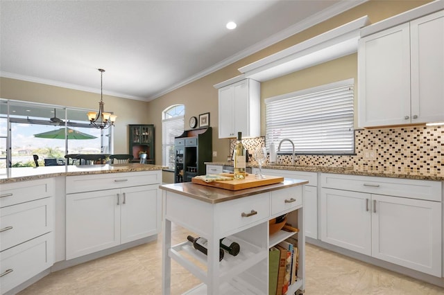 kitchen with sink, light stone counters, ornamental molding, white cabinets, and decorative light fixtures