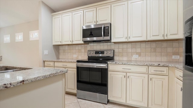 kitchen with light tile patterned floors, stainless steel appliances, light stone counters, cream cabinets, and sink