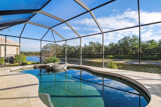 view of pool with glass enclosure, a water view, a pool with connected hot tub, and a patio area