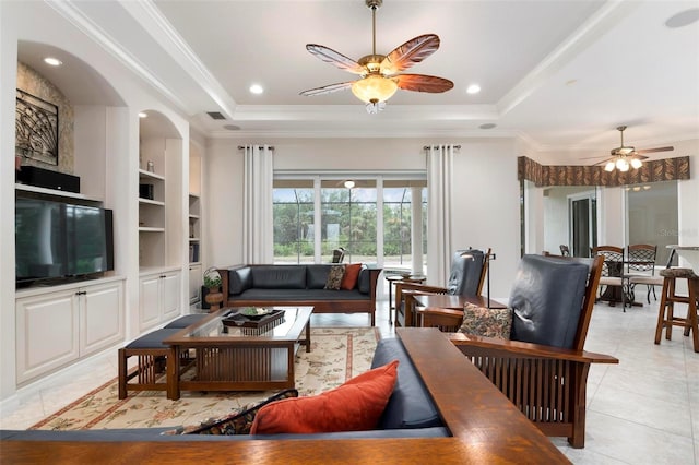 living room featuring built in shelves, crown molding, ceiling fan, and a raised ceiling