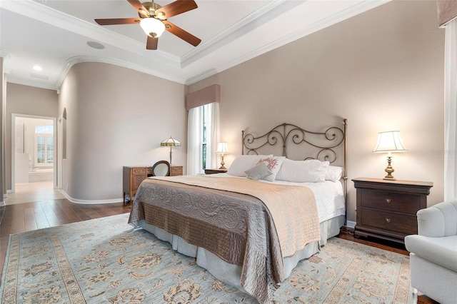 bedroom featuring ensuite bathroom, hardwood / wood-style floors, ornamental molding, ceiling fan, and a tray ceiling