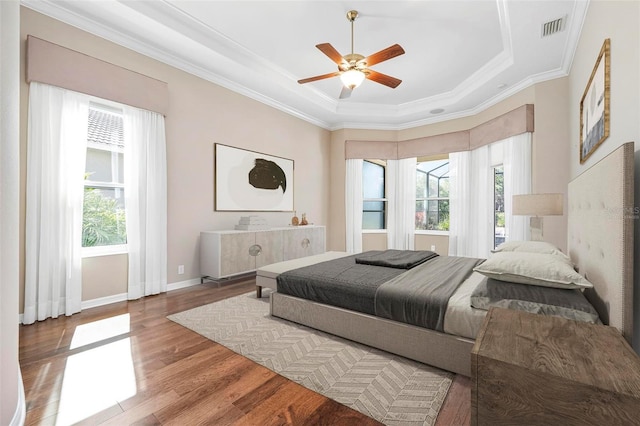 bedroom featuring visible vents, a raised ceiling, wood finished floors, and ornamental molding