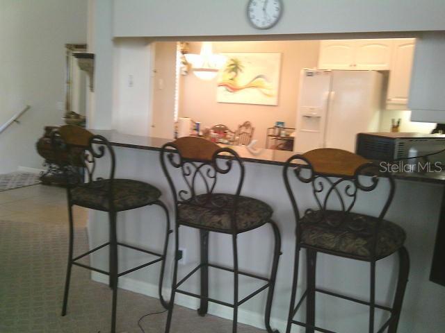 kitchen featuring a breakfast bar, white refrigerator with ice dispenser, white cabinetry, and black microwave