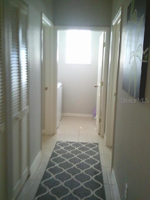 hall featuring baseboards, washer / clothes dryer, and light tile patterned flooring