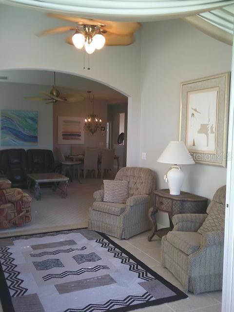 tiled living room featuring arched walkways, vaulted ceiling, and ceiling fan with notable chandelier