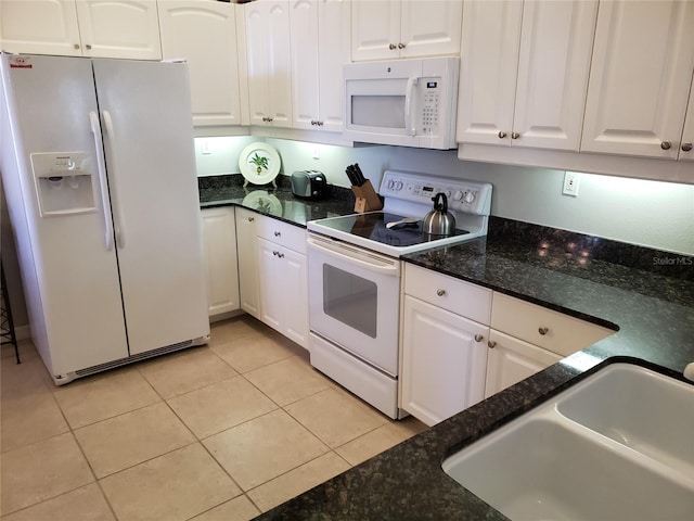 kitchen with light tile patterned flooring, white appliances, a sink, white cabinets, and dark stone counters