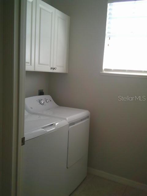 clothes washing area with tile patterned floors, washing machine and dryer, cabinet space, and baseboards