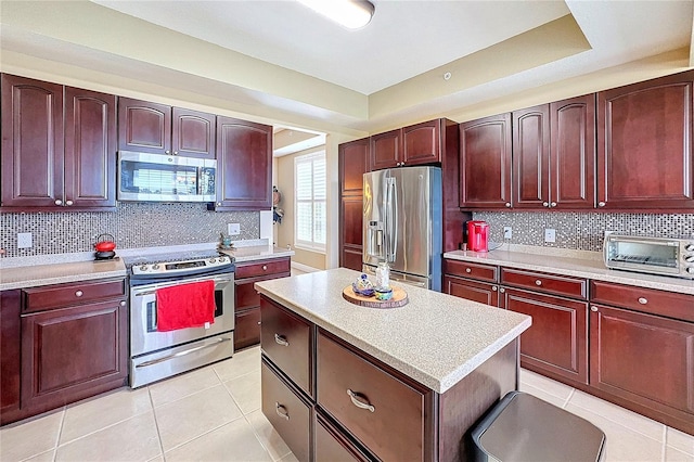 kitchen with light tile patterned floors, stainless steel appliances, decorative backsplash, a raised ceiling, and a kitchen island