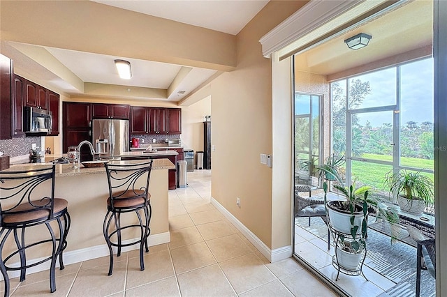 kitchen featuring decorative backsplash, a tray ceiling, appliances with stainless steel finishes, a kitchen breakfast bar, and light tile patterned floors