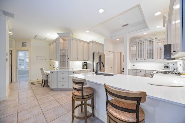 kitchen with a kitchen bar, sink, kitchen peninsula, a tray ceiling, and high end refrigerator