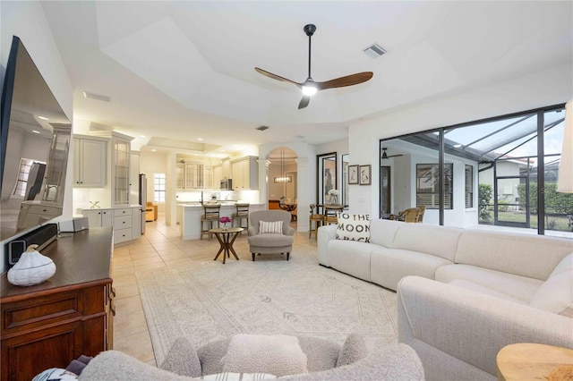 living room featuring lofted ceiling, sink, light tile patterned flooring, ceiling fan, and a tray ceiling