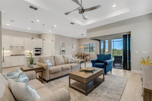 living room featuring light hardwood / wood-style floors, a tray ceiling, crown molding, and ceiling fan