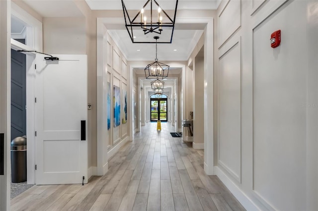 hall featuring light hardwood / wood-style flooring, ornamental molding, and an inviting chandelier