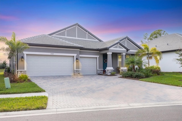 craftsman-style home with an attached garage, stone siding, a tile roof, and decorative driveway