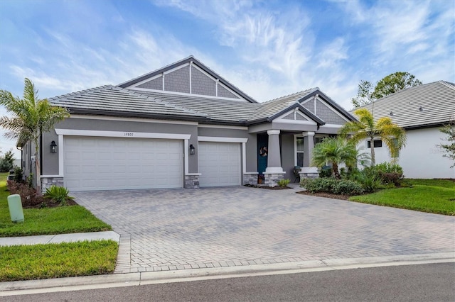 craftsman inspired home with a garage, stone siding, decorative driveway, and a tile roof