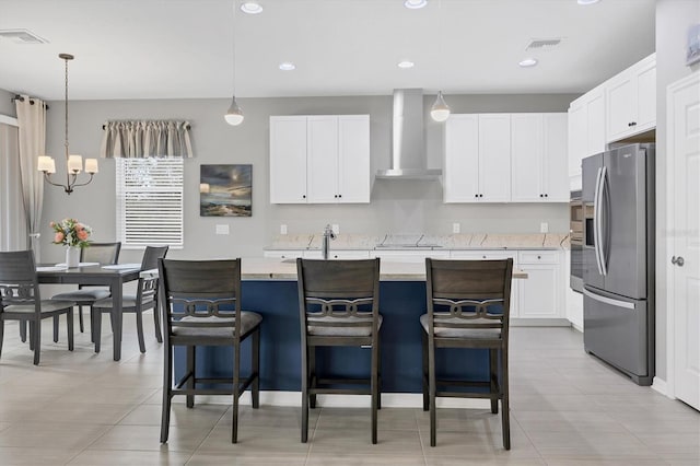 kitchen featuring visible vents, an island with sink, wall chimney exhaust hood, stainless steel appliances, and light countertops