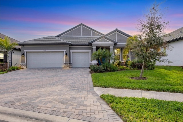 view of front of home with an attached garage, a tile roof, stone siding, decorative driveway, and a front yard