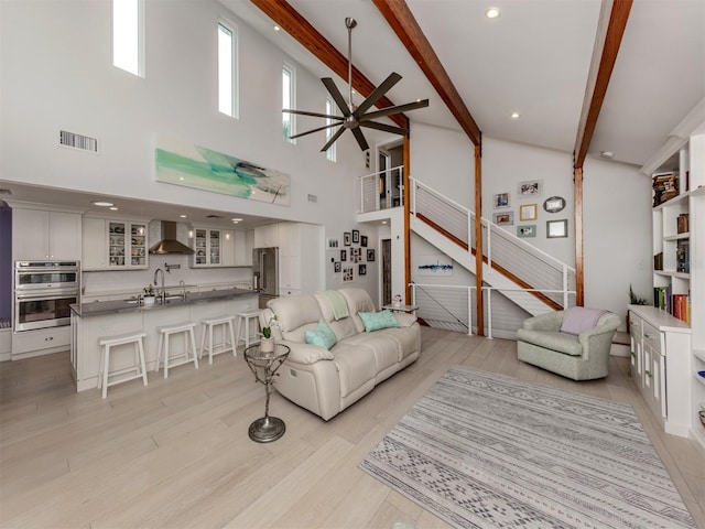 living room with ceiling fan, sink, beamed ceiling, and a high ceiling