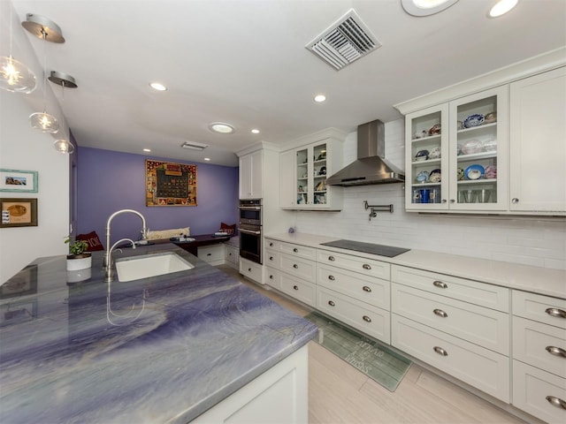 kitchen featuring sink, hanging light fixtures, white cabinets, wall chimney exhaust hood, and black electric cooktop