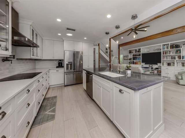 kitchen with white cabinets, wall chimney range hood, stainless steel appliances, an island with sink, and sink