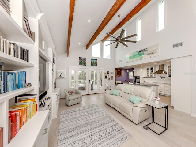 living room featuring a towering ceiling, french doors, light wood-type flooring, ceiling fan, and beam ceiling