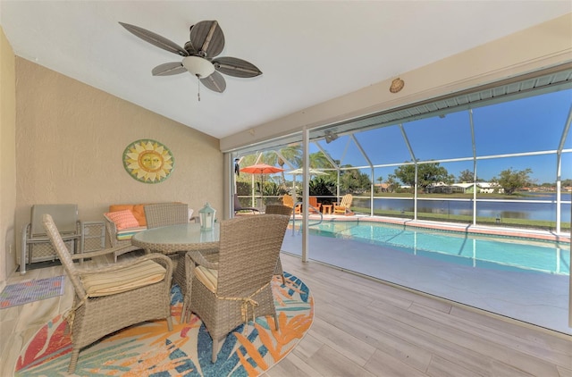 sunroom featuring a water view, ceiling fan, and a pool