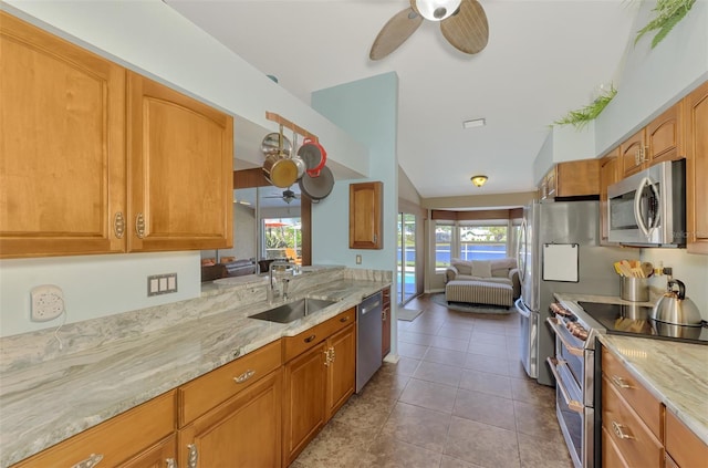kitchen featuring ceiling fan, appliances with stainless steel finishes, light stone countertops, vaulted ceiling, and a sink