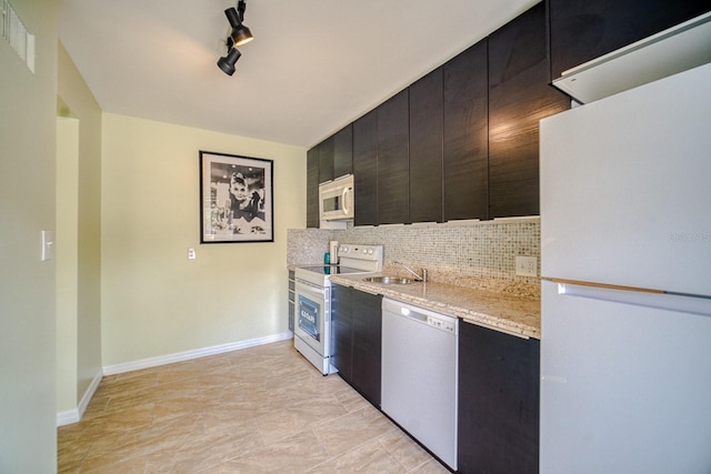 kitchen with rail lighting, tasteful backsplash, white appliances, light stone countertops, and sink