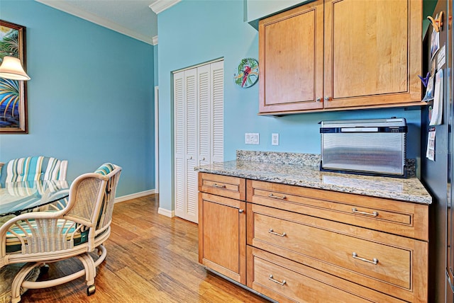 kitchen featuring crown molding, light stone countertops, and light wood-type flooring