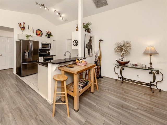 kitchen featuring lofted ceiling, white cabinetry, stainless steel appliances, kitchen peninsula, and a breakfast bar area