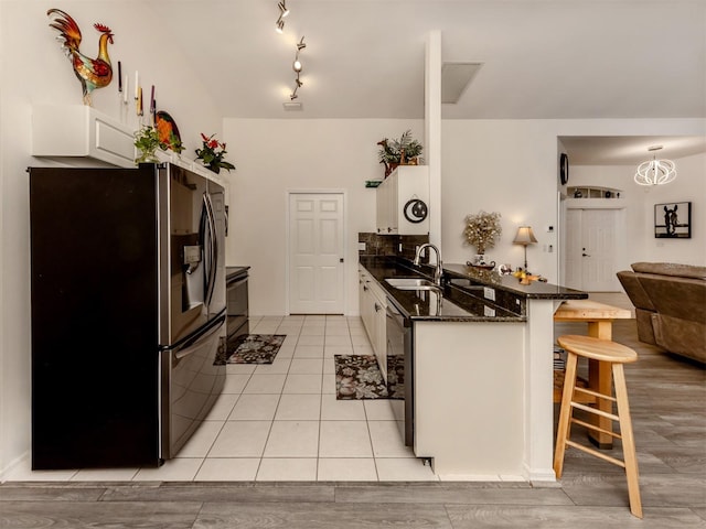 kitchen featuring white cabinets, stainless steel refrigerator with ice dispenser, sink, hanging light fixtures, and a breakfast bar area