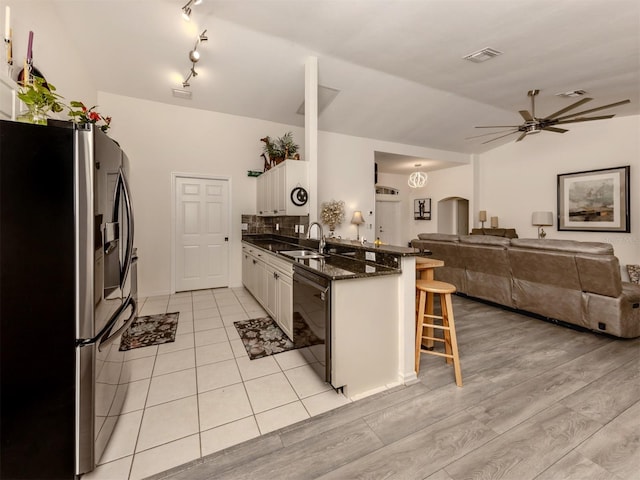 kitchen with kitchen peninsula, stainless steel fridge, white cabinets, black dishwasher, and a breakfast bar area