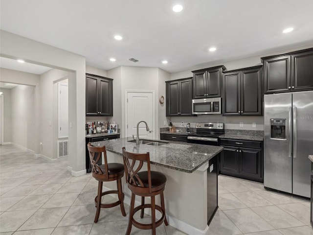 kitchen featuring appliances with stainless steel finishes, a kitchen bar, dark stone counters, an island with sink, and sink