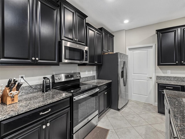 kitchen with light tile patterned floors, appliances with stainless steel finishes, and dark stone countertops