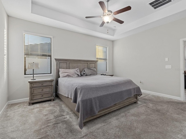 carpeted bedroom with ceiling fan and a raised ceiling