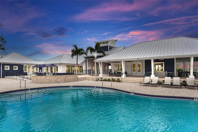 pool at dusk with ceiling fan and a patio