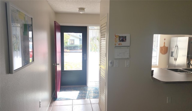 doorway to outside featuring sink, light tile patterned floors, and a textured ceiling