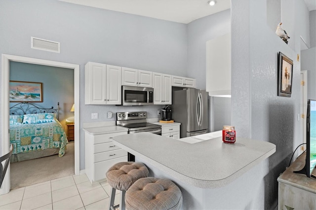 kitchen with white cabinetry, light tile patterned floors, appliances with stainless steel finishes, a kitchen breakfast bar, and kitchen peninsula