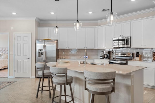 kitchen featuring appliances with stainless steel finishes, decorative light fixtures, white cabinetry, sink, and a center island with sink