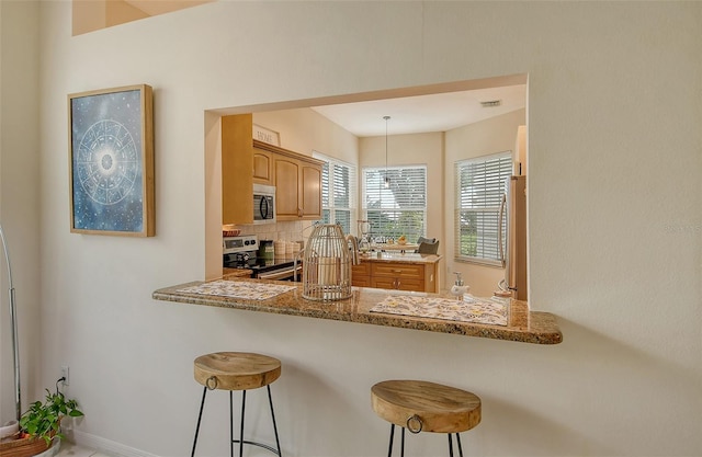 kitchen with hanging light fixtures, stainless steel appliances, light stone countertops, a kitchen bar, and decorative backsplash