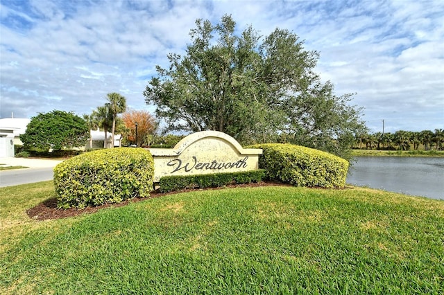 community / neighborhood sign featuring a lawn and a water view