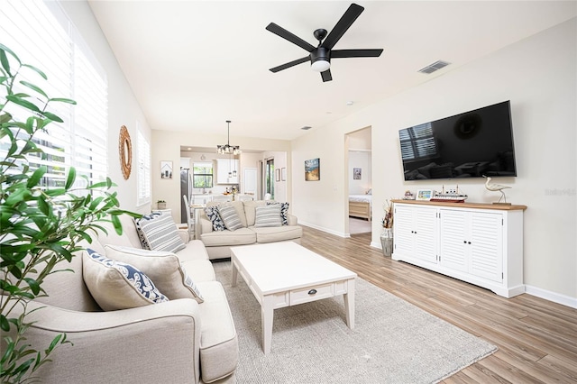 living room with ceiling fan with notable chandelier and light hardwood / wood-style flooring