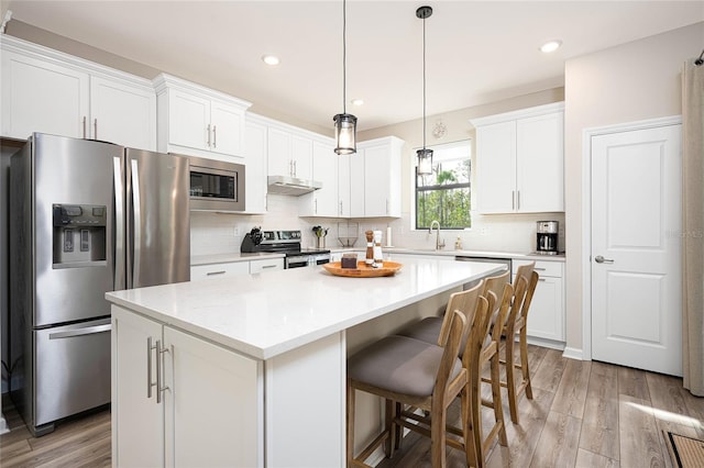 kitchen with pendant lighting, light hardwood / wood-style flooring, appliances with stainless steel finishes, white cabinetry, and a kitchen island